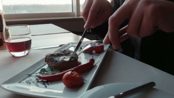 Ο άνθρωπος με ένα μαχαίρι τέμνει την μπριζόλα σε ένα πιάτο — Αρχείο Βίντεο