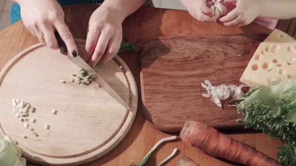 Moeder en dochter snijden UI en knoflook op een houten bord — Stockvideo