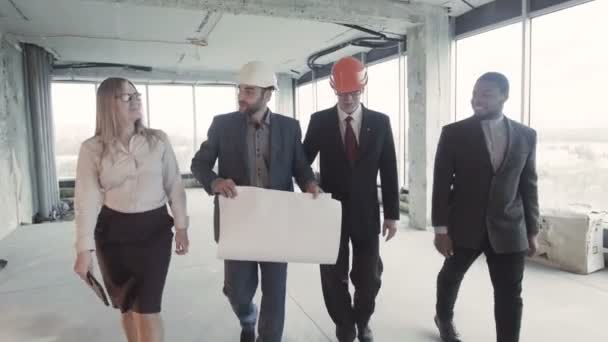 Men, woman in suit, hard hat move, communicate and discuss. Three white, one black smiling — Stock Video