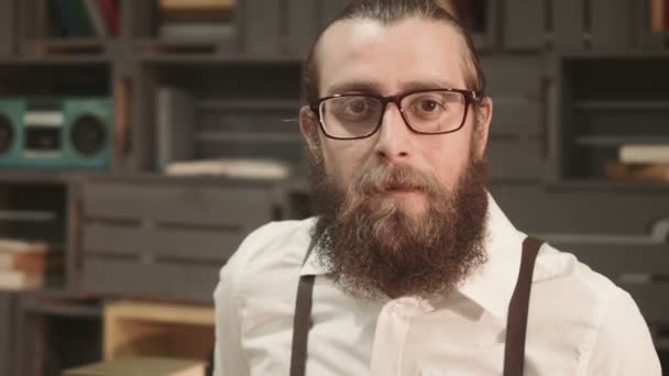 Бородатий чоловік в окулярах дивиться на камеру — стокове відео