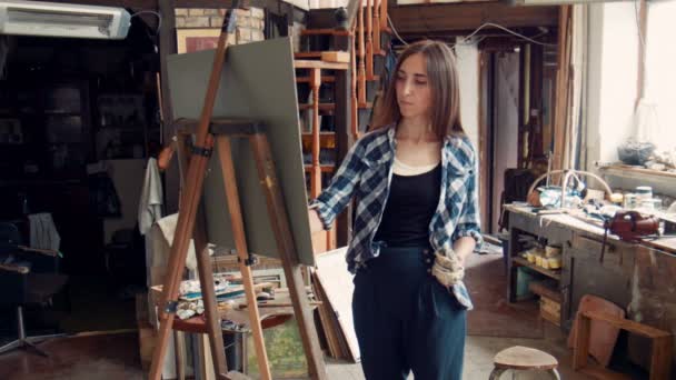 Молода жінка малює полотно в студії — стокове відео