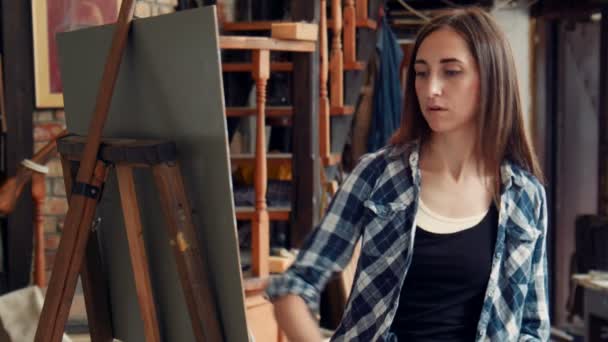 Giovane donna che dipinge una tela in uno studio — Video Stock