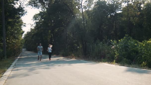 Pareja trotando a lo largo de la carretera de asfalto en el bosque — Vídeo de stock