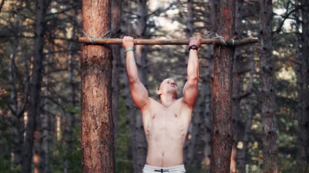 Knappe bodybuilder doen pull-ups in bos — Stockvideo