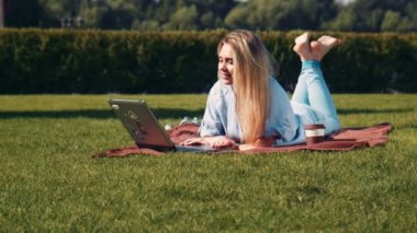 Genç kadın bir dizüstü bilgisayar kullanarak bir çim üzerinde yalan