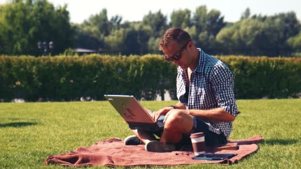 Ung man använder sin laptop utomhus på gräsmattan — Stockvideo