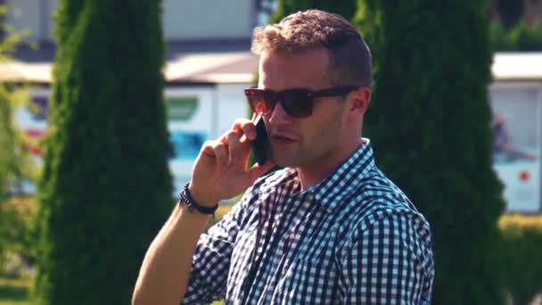 Schöner Mann mit Sonnenbrille plaudert auf einem Handy — Stockvideo