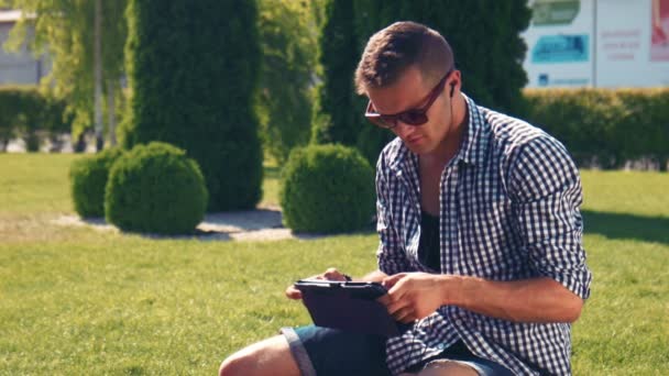 Νεαρός άνδρας σε γυαλιά ηλίου χρησιμοποιώντας μαξιλάρι στο πάρκο — Αρχείο Βίντεο