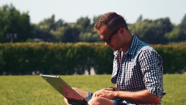 Uomo sorridente in occhiali da sole utilizzando il computer nel parco — Video Stock