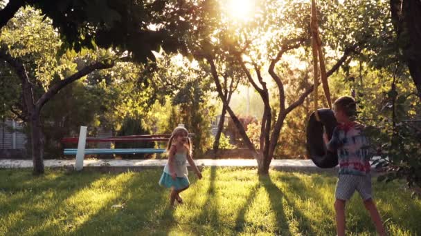 Счастливые девочка и мальчик играют в парке на качелях — стоковое видео