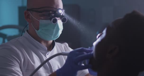 Dentista concentrato che cura il paziente etnico in clinica — Video Stock