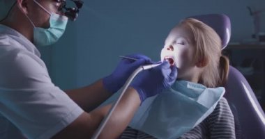 Dişçi hoparlörlü bir adam bir kızın dişini tedavi ediyor