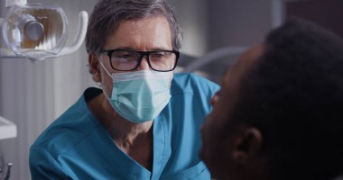 Etnik hastanın dişlerini muayene eden olgun bir diş doktoru.