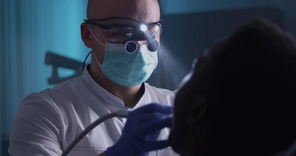 Dentista concentrato che cura il paziente etnico in clinica — Foto Stock