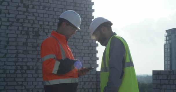 Constructor con tableta discutiendo construcción con compañero de trabajo — Vídeo de stock