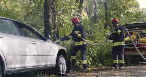 Bombeiros com mangueiras perto de carro quebrado — Vídeo de Stock