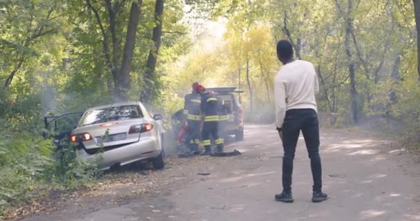 Black injured man watching firemen checking victims in car — Stock Video