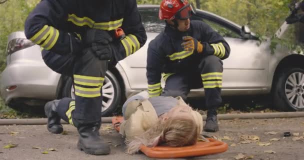 Hasiči pomáhají zraněné ženě a hašení požáru na autě — Stock video