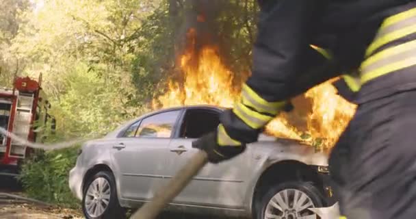 Anonieme brandweerlieden blussen vuur op auto in de buurt van bomen — Stockvideo