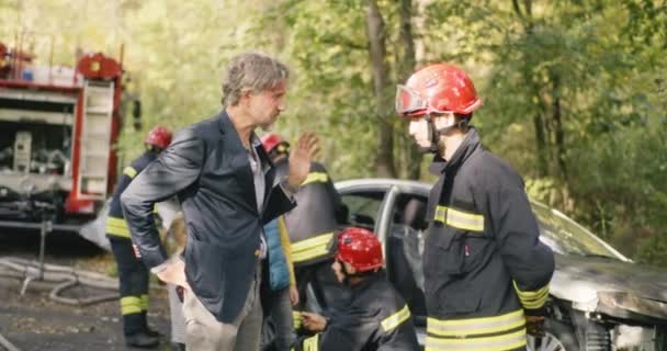 Тощий взрослый мужчина рассказывает пожарному об автокатастрофе — стоковое видео