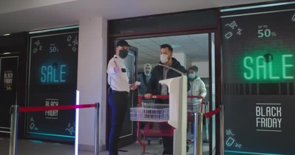 Clientes desinfectando manos mientras caminan más allá de la guardia en el centro comercial — Vídeos de Stock