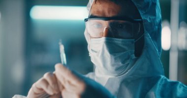 Koruyucu giysili doktor aşı enjeksiyonu hazırlıyor.