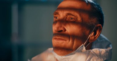 Yorgun, olgun bir doktor koruyucu elbisesini çıkarıyor.