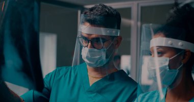Röntgen taraması yapan çok ırklı doktorlar yüz kalkanlarında.