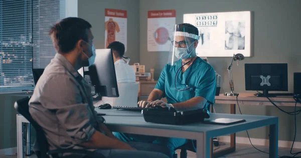 Врач-мужчина за компьютером и разговаривает с пациентом — стоковое фото