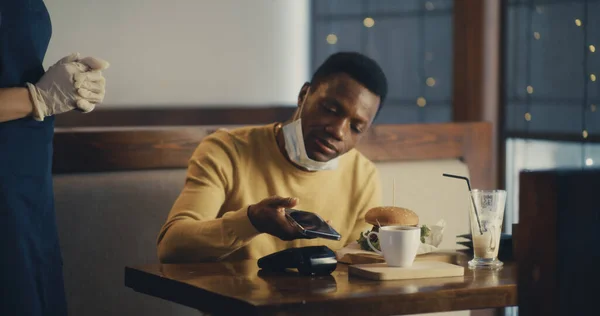 Homem preto pagando com smartphone para a ordem no café — Fotografia de Stock