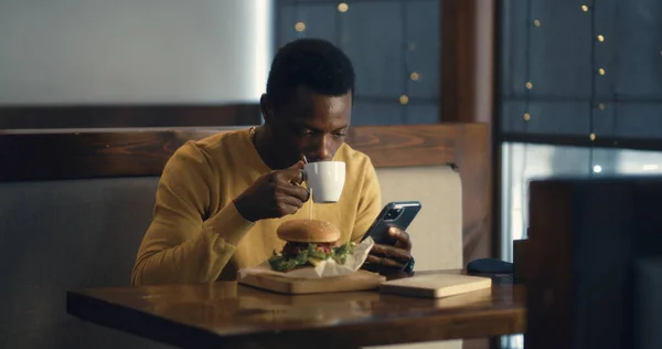 Black guy having meal in cafe after pandemic and using phone
