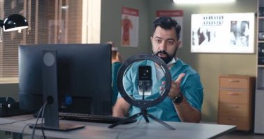 Sakallı erkek doktor iş arkadaşlarına video çağrısı yapıyor.