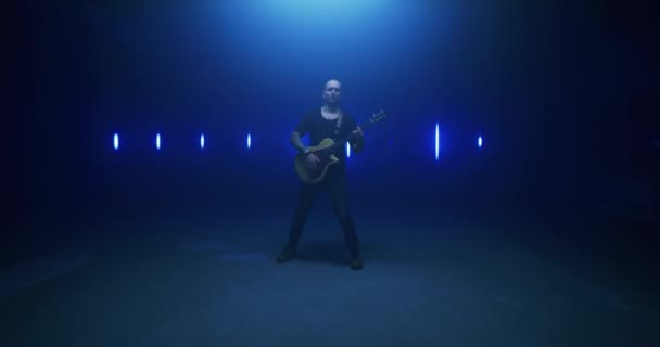 Чоловічий рокер грає на гітарі та співає пісню в темній кімнаті — стокове відео