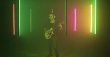 Neşeli rockçı renkli aydınlatma altında gitar çalıyor