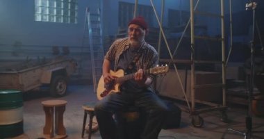 Sakallı gitarist garajda içten bir şarkı söylüyor.