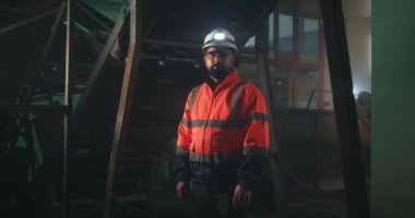 Makinelerin yanındaki kameraya bakan erkek mühendis