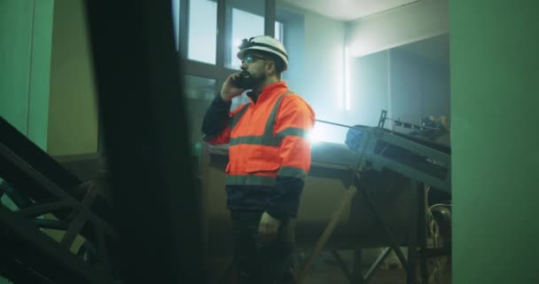 Factory worker speaking on smartphone near conveyor belt — Stock Video