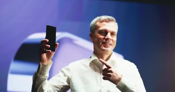 Homem maduro apontando para novo smartphone durante a apresentação — Vídeo de Stock