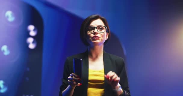 Falante feminino com novo smartphone falando contra tela LED — Vídeo de Stock