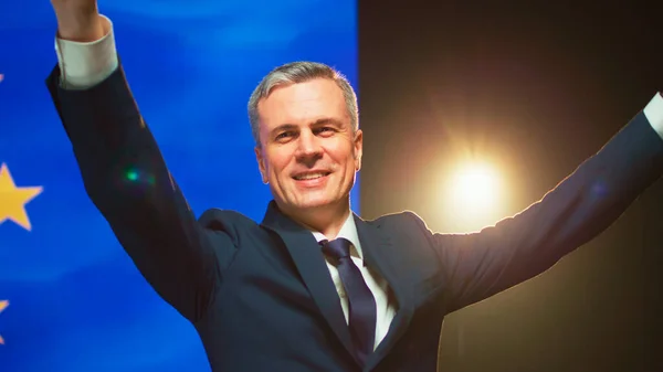 Mature politician waving hand from stage