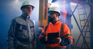 Erkek mühendisler fabrika tabletindeki verileri tartışıyor