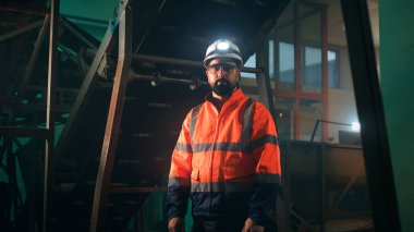 Makinelerin yanındaki kameraya bakan erkek mühendis