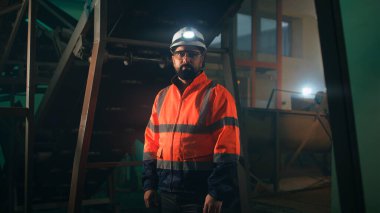 Makinelerin yanındaki kameraya bakan erkek mühendis