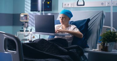 Hastane koğuşunda dizüstü bilgisayar kullanan küçük hasta.