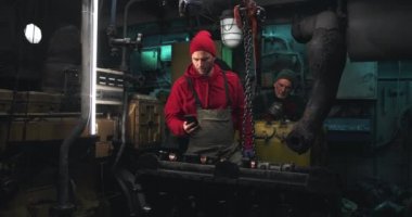 Gemi motorunu tamir eden ve akıllı telefondan konuşan adam.