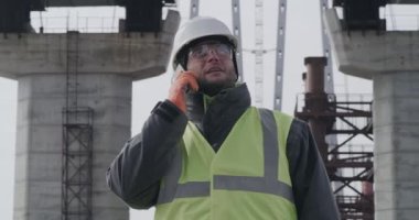 Köprüyü inceleyen ve cep telefonuyla konuşan erkek mühendis.