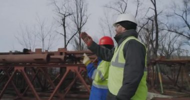 Metal yapıların yanında yürüyen ve konuşan erkek köprü yapımcıları.