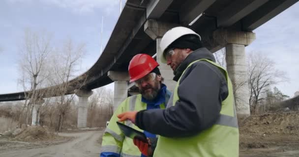 Αρσενικοί οικοδόμοι με tablet συζητώντας δεδομένα στα περίχωρα — Αρχείο Βίντεο