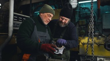 Erkek teknisyenler motor parçalarını birlikte inceliyor.