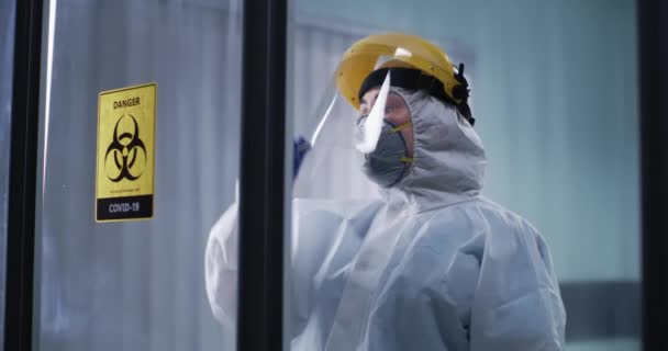 Nainen lääkäri lepää lähellä lasiseinää COVID osastolla — kuvapankkivideo